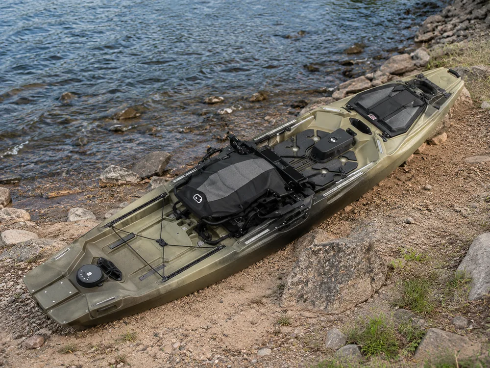 Overhead view of an olive fishing kayak on a rocky shore showing the full deck, seat, tracks and hatches