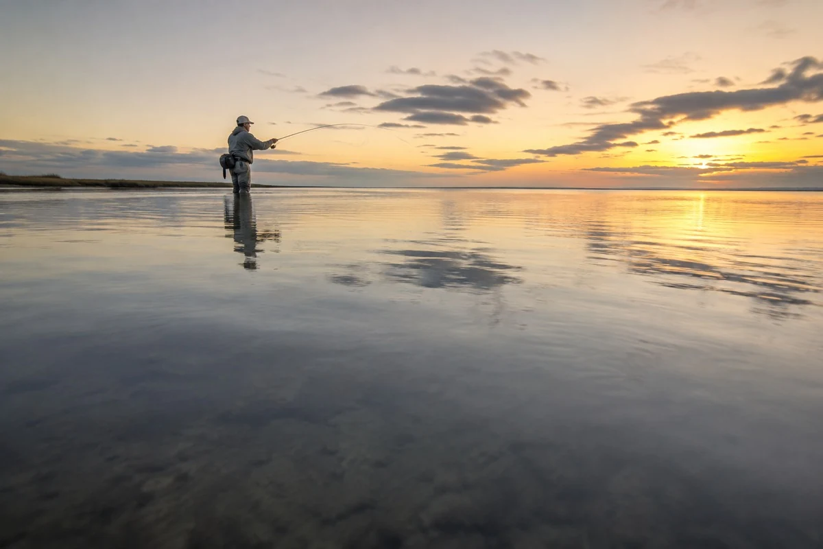 An angler wading a shallow flat at sunrise